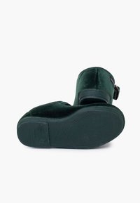 Zielone aksamitne botki sięgające kostki z masywnym obcasem i boczną klamrą, posiadające teksturowaną gumową podeszwę zapewniającą przyczepność i stabilność.