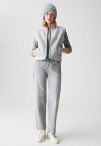 Lichtgrijze schapenvachtvest met een ritssluiting en zakken over een grijze lange mouwen shirt en lichtgrijze rechte spijkerbroek, gecombineerd met witte sneakers.