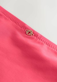 Roosa kangas sujuva tekstuuriga, millel on eristuv kuldne riistvara detail õmblusel. Õmblus on serval nähtav.