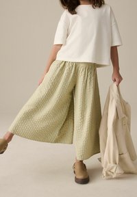 Culottes amples à rayures vertes et crème avec une taille élastique, associées à un top blanc à manches courtes et des sabots marron.