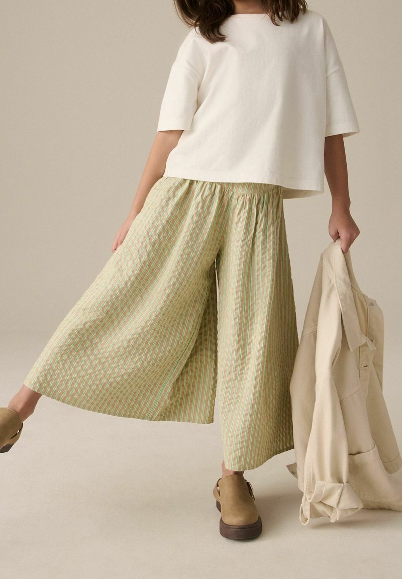 Culottes amples à rayures vertes et crème avec une taille élastique, associées à un top blanc à manches courtes et des sabots marron.