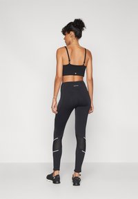 Ensemble de brassière de sport noire et de leggings. La brassière a des bretelles fines ; les leggings présentent des panneaux en maille et des accents réflecteurs. Les deux sont fabriqués dans un matériau extensible.