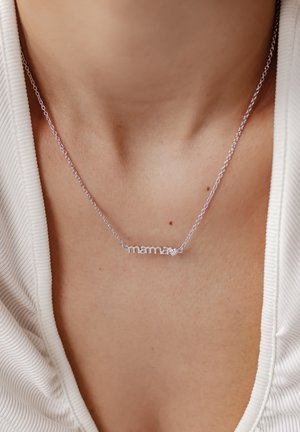 Silberne kettenglatte Halskette mit dem Wort "mama" in einer sanften Schreibschrift, geschmückt mit einem kleinen Herzakzent, die auf nackter Haut liegt.
