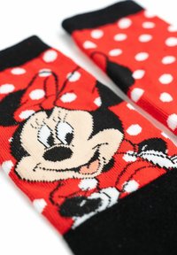 Calze rosse con una grafica in bianco e nero di un personaggio dei cartoni animati con un papillon a pois, accentuate da macchie bianche sullo sfondo rosso.