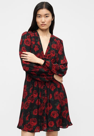 Μαύρο φόρεμα με βαθύ V-λαιμόκοψη, διακοσμημένο με σχέδια από κόκκινες τριανταφυλλιές. Μακριά, φουσκωτά μανίκια και ελαφρώς ανοιχτό τελείωμα, με λεπτομέρειες από κουμπιά.