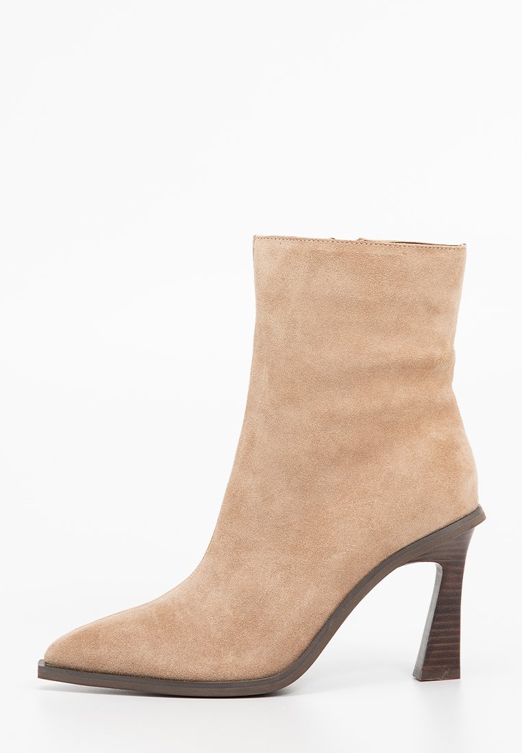 Botín de ante beige hasta el tobillo con punta afilada y un alto tacón de madera apilada. Textura suave con un diseño limpio y minimalista.