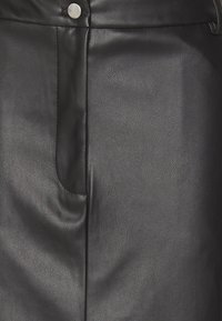 Svart konstläderkjol med en texturerad yta, en synlig ficka och en metallknappstängning i midjan. Slät, stilren finish.