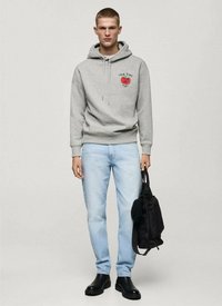 Felpa grigia con una grafica di una mela rossa e il testo "NEW YORK", abbinata a jeans azzurri chiari e stivaletti neri, mentre tiene una borsa nera.
