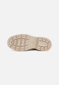 Semelle de chaussure en caoutchouc beige avec un motif de grip texturé, présentant des rainures distinctes et une section de talon circulaire. Marquée 'Tamaris' et taille 37.
