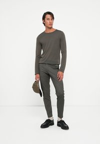 Long-sleeve, olive green shirt paired with tailored gray checkered trousers. Accessories include a black striped cap and black shoes.