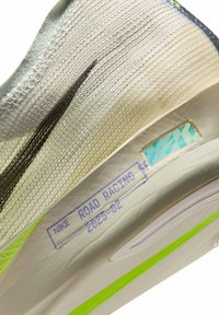 Nike hardloopschoen met een gestructureerde, lichtgrijze mesh bovenkant, zwarte accenten en een versterkte zool met een reflecterende, groene streep.