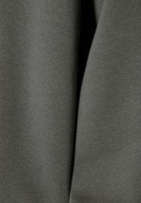 Primo piano di un tessuto grigio scuro che mostra una fine trama a maglia e morbide pieghe con leggeri ombreggiamenti tra le pieghe.