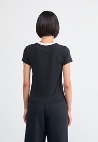 Fekete rövid ujjú póló fehér kerek nyakkivágással. Puha pamut anyag; testhezálló kialakítás sima textúrával, minta és látható fémrészek nélkül.