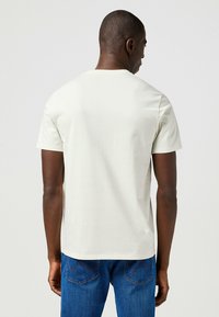 Camiseta corta de manga corta en gris claro con cuello redondo. Confeccionada en una tela suave, presenta un diseño sencillo sin patrones. Llevada con jeans azules.