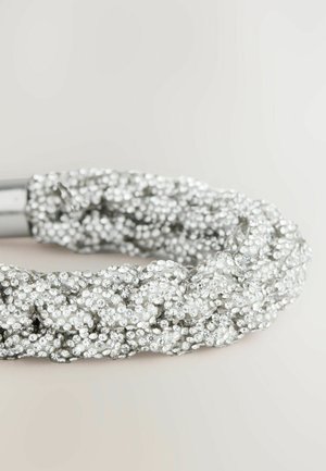 Hopeaketjupanta, joka on päällystetty pienillä, kimaltelevilla strasseilla, sisältää kiiltävän metallisoljen, jossa on teksturoitu pinta ja monimutkainen muotoilu.