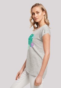 Tricou gri din bumbac cu mâneci scurte, având un grafic cu cochilii verzi și bule pe parte frontală. Purtați cu pantaloni albi ajustați.