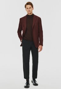 Burgundowa marynarka nałożona na brązowy golf, w połączeniu z czarnymi spodniami i czarnymi butami na sznurówki, charakteryzującymi się slim-fit i gładką teksturą.