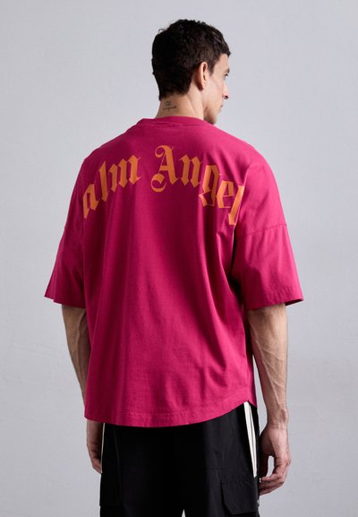 Rosa Baumwolloversized-T-Shirt mit großen orangen Gothic-Schriftzug "Palm Angel" auf der Rückseite, kurzen Ärmeln und entspannter Passform.