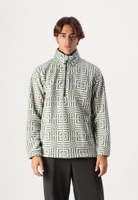 Fleece pullover met een hoge kraag, gekenmerkt door een geometrisch patroon in blauwe en crèmekleurige tinten, met een ritssluiting aan de voorkant en lange mouwen.