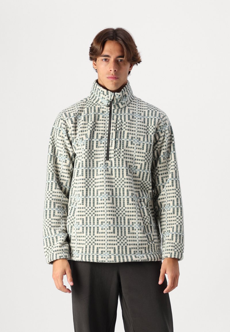 Fleece pullover met een hoge kraag, gekenmerkt door een geometrisch patroon in blauwe en crèmekleurige tinten, met een ritssluiting aan de voorkant en lange mouwen.