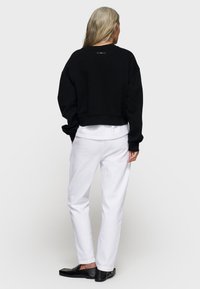 Czarny krótki sweatshirt o luźnym kroju, z szerokimi rękawami i małym logo widocznym z tyłu, zestawiony z białymi spodniami o prostym kroju.