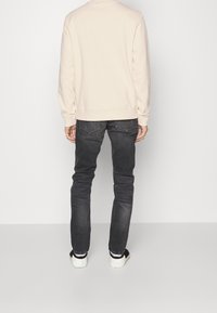 Sudadera color beige claro, jeans grises y zapatillas. Tela suave, puños y cintura acanalados. Diseño simple con un corte casual y acentos oscuros.