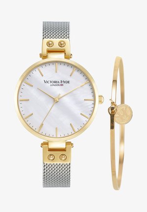 Reloj de tono dorado con una correa de malla plateada, esfera de nácar blanco, delgados índices horarios dorados y una pulsera bangle dorada a juego.
