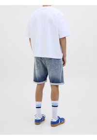 T-shirt bianca oversize, pantaloni corti in denim scoloriti con orli arrotolati, calze bianche fino al ginocchio con strisce blu e sneakers blu con suole beige.