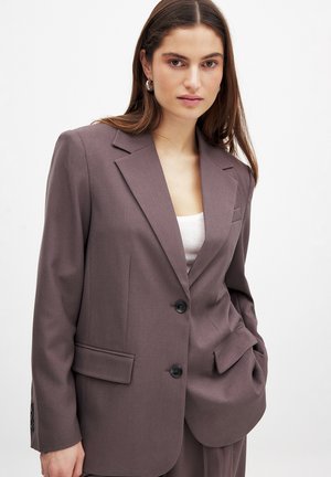 Blazer lavande en tissu texturé, avec un revers cranté, deux poches avant et deux boutons. Coupe ajustée avec des détails subtils.