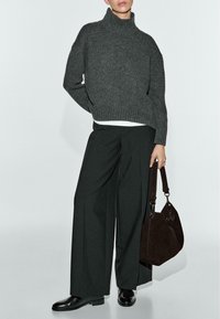 Maglione grigio a collo alto lavorato a maglia, pantaloni neri a gamba larga e stivaletti neri alla caviglia. Borsa in camoscio marrone con doppio manico e dettagli in metallo.