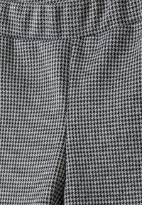 Tejido con patrón de pata de gallo en blanco y negro con una textura tejida. Presenta una cinturilla elástica y un acabado suave.