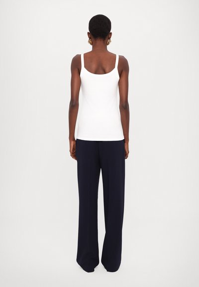 Hvit ribbestrikket tanktopp med tynne stropper, kombinert med marineblå vide bukser, sett fra baksiden. Jevn tekstur i stoffet, minimalistisk design.