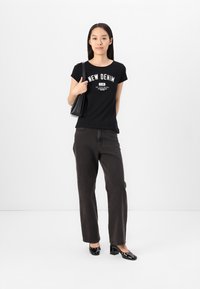 Melnas short-sleeve T-krekls ar "NEW DENIM" grafiku, apvienots ar tumši pelēkām plati kājām džinsiem un melniem augstpapēžu apaviem. Minimalistisks pleca soma.