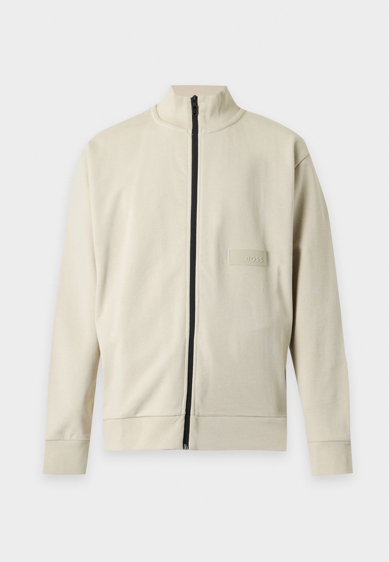 Beige langärmelige Jacke mit schwarzem Reißverschluss und kleinem rechteckigem BOSS-Logo-Patch auf der linken Brust.