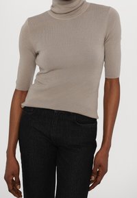 Top beige de cuello alto acanalado con mangas cortas, silueta ajustada, textura suave, combinado con jeans oscuros de mezclilla.