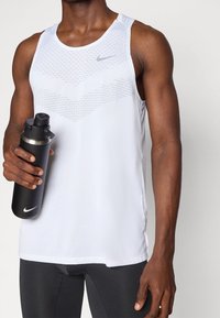 Valkoinen Nike-hihaton paita, jossa on verkkomainen muotoilu ja huomaamaton logo, yhdistettynä mustaan vesipulloon, jossa on harmaa kansi ja kaareva muoto.