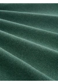 Tessuto verde testurizzato con una superficie intrecciata, che presenta una finitura morbida e opaca, piegato in più strati, creando profondità e dimensione.
