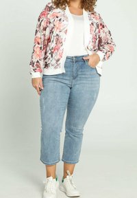 Cárdigan de estampado floral en tejido suave, con puños blancos, combinado con vaqueros cortos de color azul claro y zapatillas blancas con detalles en verde.