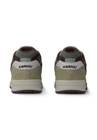 Bruna och gröna sportskor med överdel i mocka och mesh, vit hälaccent, grå tunga och dämpad sula. KARHU-logotyp på hälen.