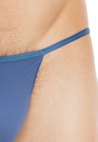 Blauer Bikini mit dünnem Träger, aus glattem Stoff mit minimaler Abdeckung, der den Hautton darunter zeigt und eine subtile Textur aufweist.
