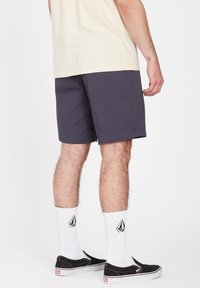 Gray shorts with a relaxed fit, side pockets, and visible stitching details. Worn with white patterned socks and black slip-on shoes.