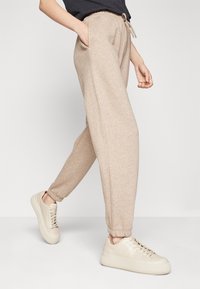 Beżowe spodnie dresowe z elastycznym pasem i bocznymi kieszeniami, zestawione z jasnymi trampkami o gładkiej fakturze i sznurowanym fasonie.