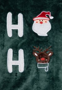 Tmavě zelená látka s bílým vyšitým písmem "H" a motivem Santa Clause a sobů s červenými a hnědými akcenty.