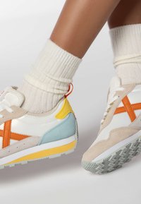 White and beige sneakers with orange and blue accents, textured suede and leather materials, rubber sole, and zigzag pattern on the bottom.
