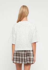 Ανοιχτό γκρι πουλόβερ με κοντά μανίκια και υφή πλεκτού μοτίβου, συνδυασμ ένο με φούστα καρό σε καφέ και λευκές αποχρώσεις.