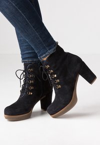 Czarne zamszowe botki za kostkę na grubym obcasie, z ozdobnymi złotymi oczkami, sznurowadłami oraz bocznym zamkiem błyskawicznym dla łatwego zakładania.