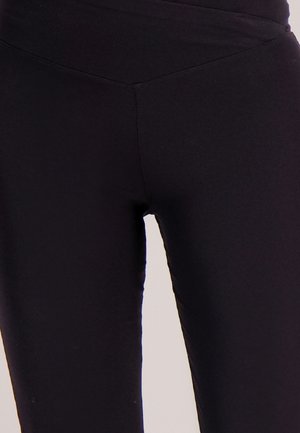 Zwarte legging van een rekbaar, glad materiaal met een hoge tailleband. Het ontwerp is nauwsluitend, zonder zichtbare patronen of accessoires.