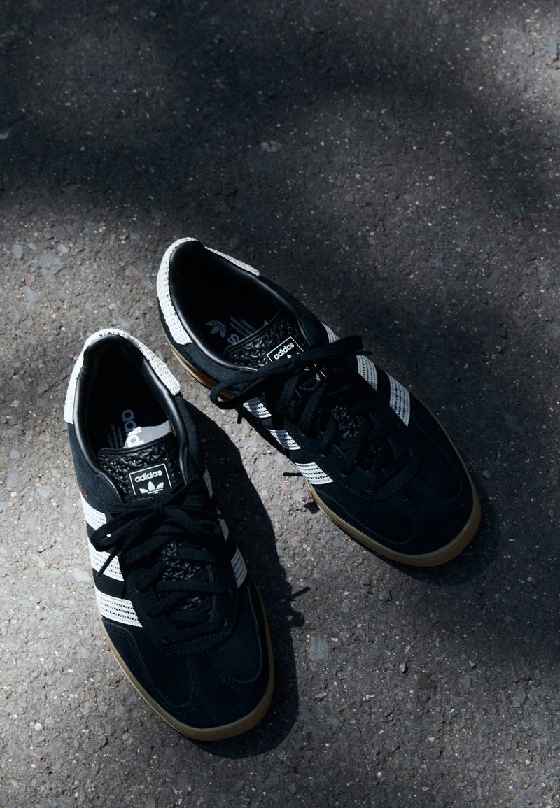 Zwarte suède sneakers met witte strepen, rubberen zolen en zwarte veters. Logo op de tong en textuurelementen op de hiel.