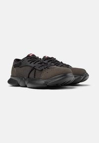 Black athletic shoes with a mesh upper and suede details, rounded sole, and black laces. Features subtle branding in red.