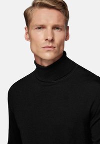 Black turtleneck sweater in textured knit fabric, featuring a high collar and fitted design. Visible ribbed detailing at the neckline.